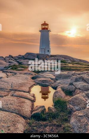 Un coucher de soleil doré jette une lueur sereine sur le phare de Peggy's Cove, construit en 1915. Le couple connecté profite de la vue paisible. Banque D'Images