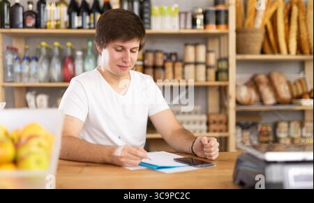 Jeune vendeur masculin prenant des notes dans les documents Banque D'Images