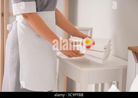 Jeune femme de chambre mettant des serviettes propres et des fleurs de plumeria rose sur la table de chevet dans la chambre d'hôtel, gros plan Banque D'Images