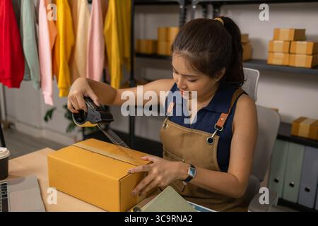 Jeune femme entrepreneure scellant soigneusement le paquet avec du ruban adhésif, préparant les commandes de marchandises, gérant l'expédition et la livraison pour son succès en ligne Banque D'Images