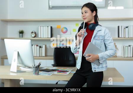 Jeune femme réfléchie dans le bureau moderne avec tablette et casque Banque D'Images