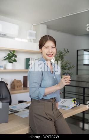 Jeune femme joyeuse dans le bureau élégant tenant le café Banque D'Images