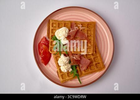 Gaufres délicieusement confectionnées avec garniture fouettée crémeuse, Arugula fraîche et Prosciutto savoureux, présentées sur une assiette élégante Banque D'Images