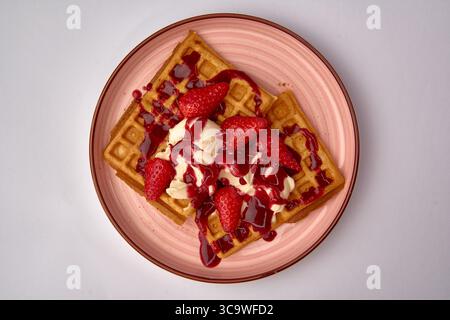 Gaufres délicieusement savoureuses garnies de fraises fraîches et de crème, assaisonnées de sauce aux baies dans une assiette élégante Banque D'Images