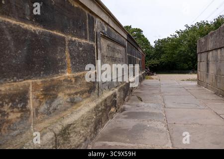 Vue rapprochée d'un mur de pont en pierre avec texte gravé et une passerelle pavée pour piétons sous un ciel couvert Banque D'Images