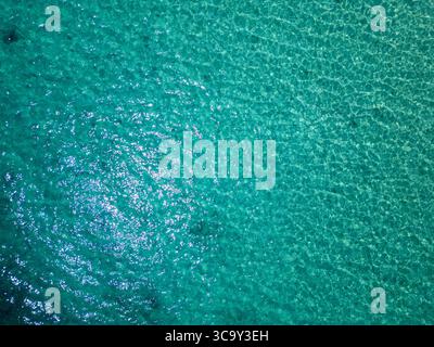 Vue aérienne de la mer turquoise scintillante avec des rochers sous-marins visibles à travers l'eau claire. Surface paisible reflétant la lumière du soleil lors d'une journée d'été calme Banque D'Images