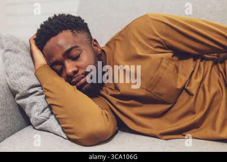 Fatigué jeune homme africain dormant paisiblement sur un canapé dans sa maison confortable. Banque D'Images