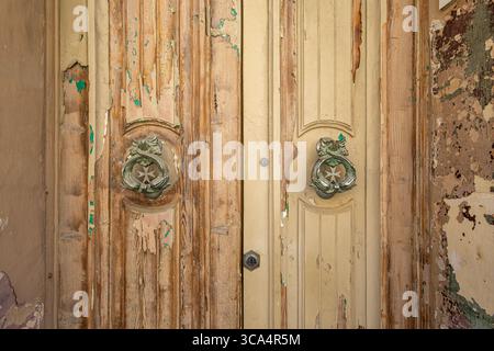 Détail de double porte en bois. Peeling peinture et deux frappeurs de porte avec des dauphins jumeaux et la croix maltaise., Sliema, Malte. Banque D'Images