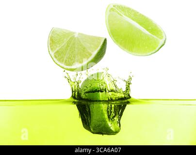 Citrons verts frais tombant dans la boisson éclaboussante sur fond blanc Banque D'Images