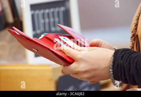 Gros plan d'une femme tenant un portefeuille rouge ouvert, se préparant à payer avec une carte au marché de fermiers en plein air. Style de vie urbain et shopping moderne dans authentique Banque D'Images