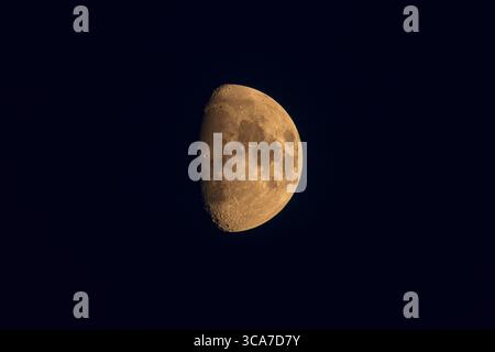 Gros plan d'une lune gibbous cirée brillante avec des tons dorés chauds sur un ciel nocturne sombre. Banque D'Images