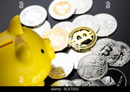 Une tirelire jaune entourée de pièces d'argent et d'or Bitcoin sur une surface noire. L'image symbolise la monnaie numérique, l'épargne financière et l'inve Banque D'Images