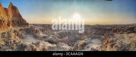 Une vue panoramique sur un paysage désertique au coucher du soleil, avec le soleil brille brillamment sur des formations rocheuses érodées. Banque D'Images