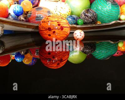 SEATTLE - APR 25, 2025 - sphères de verre colorées de différentes tailles et motifs reposant dans un conteneur en forme de bateau, reflétant la lumière vibrante dans l'obscurité Banque D'Images