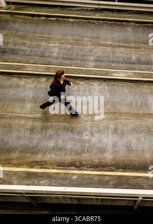 Une femme en costume noir court sur une surface en béton. Banque D'Images
