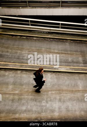 Une femme en costume noir court sur une surface en béton. Banque D'Images