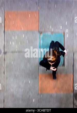 Une photo au-dessus de la tête d'une personne vêtue de vêtements noirs, peut-être une femme, debout sur une surface avec des sections orange et grises. La personne regarde vers le bas, et Banque D'Images