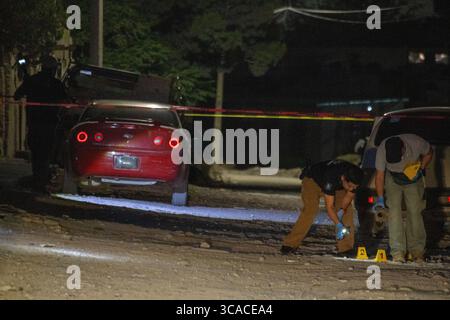 L'équipe médico-légale sonde la scène de crime nocturne près d'une voiture rouge à Ciudad Juarez, victime de violence. Banque D'Images