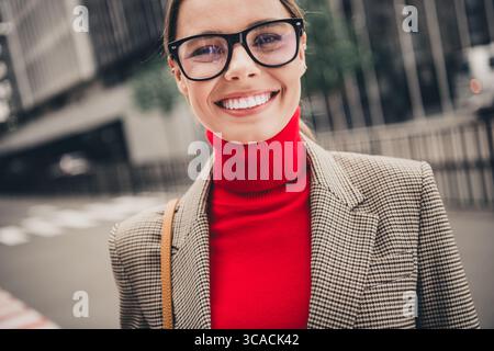 Jeune femme d'affaires élégante dans un environnement urbain portant un élégant col roulé rouge et blazer à carreaux avec un sourire charmant Banque D'Images