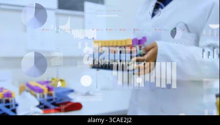 Tenant le scientifique dans la blouse de laboratoire analysant le portoir de tubes à essai sanguin dans le laboratoire avec des superpositions de données numériques Banque D'Images