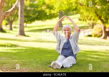 Femme senior étirant les jambes croisées sur la pelouse d'herbe dans le parc ensoleillé portant des vêtements de sport Banque D'Images