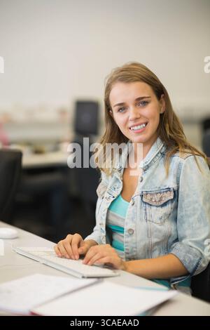 Travailleuse portant une veste en denim tapant sur le clavier au bureau du laboratoire informatique avec moniteur et papiers Banque D'Images