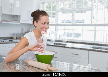 Femme dans la trentaine fouettant des ingrédients dans un bol vert sur le comptoir de granit dans la cuisine à la maison Banque D'Images