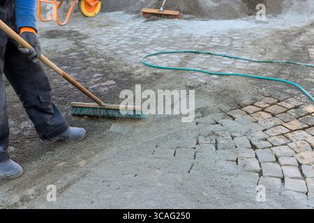 L'ouvrier nettoie la rue pavée à l'aide d'outils de balai dans des conditions de journée de travail dans la zone de construction. Banque D'Images