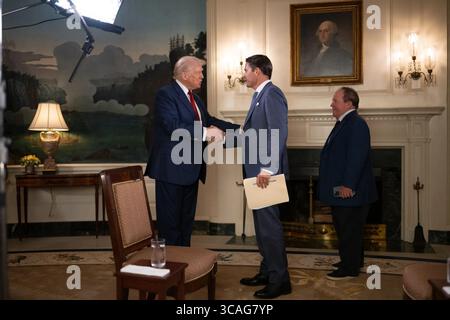 Le président Donald Trump serre la main de Rob Finnerty de Newsmax suite à leur interview à la Maison Blanche le 1er août 2025, en présence d’un assistant. Image reproduite avec l'aimable autorisation de la Maison Blanche. Banque D'Images