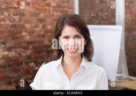 Femme adulte souriant tout en se tenant devant un mur de briques rouges avec tableau de conférence vierge Banque D'Images