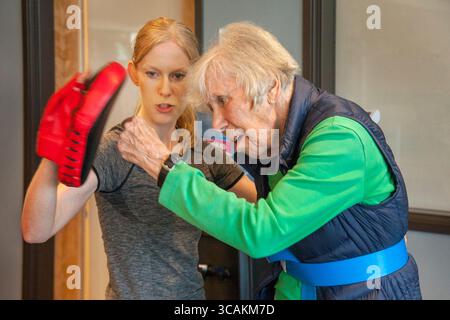19 juillet 2017 : une femme enthousiaste de 87 ans pratique des coups de poing avec un instructeur tenant un gant d'entraînement dans un gymnase du centre senior à Huntington Beach, CA. (Crédit image : © Spencer Grant/ZUMA Press Wire) Banque D'Images