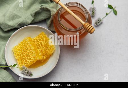 Nid d'abeille frais et pot de miel avec une benne en bois sur une table en marbre, décorée de fleurs et de tissu vert Banque D'Images