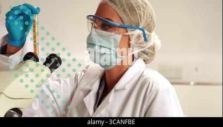 Examinateur scientifique tenant le tube d'échantillon dans la main gantée à hauteur des yeux sur la paillasse de laboratoire, avec microscope Banque D'Images