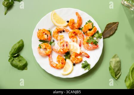 Cuisson de crevettes frites avec épices aromatiques et citron dans une assiette isolée sur vert. Banque D'Images
