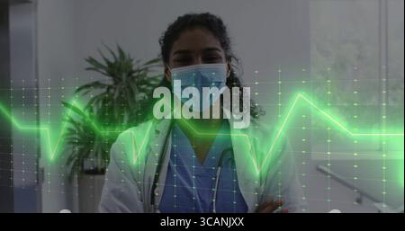 Travailleur médical portant un masque chirurgical, une blouse blanche et un stéthoscope dans le couloir, montrant la superposition ECG Banque D'Images