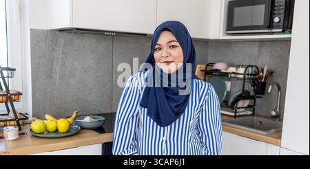 Femme musulmane debout dans la cuisine moderne portant le Hijab Banque D'Images
