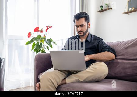 Homme utilisant un ordinateur portable tout en étant assis sur un canapé à la maison Banque D'Images