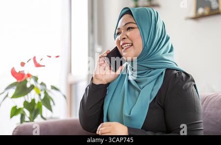 Femme musulmane heureuse utilisant le téléphone portable à la maison Banque D'Images