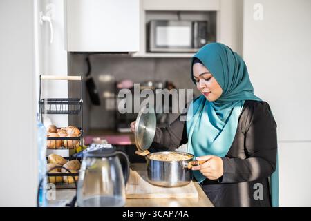 Femme musulmane debout dans la cuisine moderne portant le Hijab Banque D'Images