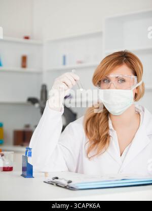 Scientifique inspectant l'écouvillon au niveau des yeux sur une paillasse de laboratoire avec presse-papiers, portoir à tubes et bécher rouge Banque D'Images