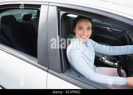 Conducteur féminin souriant et reposant sur le volant en berline blanche avec sièges en cuir, espace copie Banque D'Images