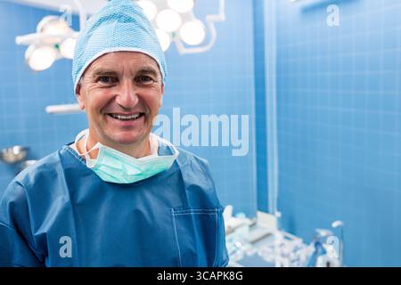 Chirurgien masculin senior debout OU portant des gommages bleus, casquette sous les plafonniers, espace de copie Banque D'Images