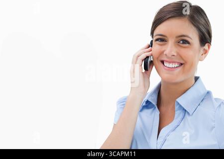 Femme professionnelle en chemise bleu clair souriant et tenant smartphone à l'oreille dans le studio, espace de copie Banque D'Images