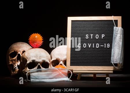 Concept de coronavirus COVID-19. Crânes humains avec masque et modèle de virus près du papier à lettres avec des mots ARRÊTENT COVID-19 sur fond sombre Banque D'Images