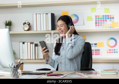 Heureuse jeune femme appréciant la musique tout en travaillant sur smartphone Banque D'Images