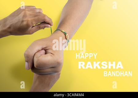 Mains humaines attachant rakhis colorés au poignet, avec un fond coloré, célébrant le lien de l'amour et de la protection. Concept du Raksha Bandhan Banque D'Images