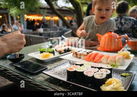 Sélection de sushis frais comprenant des rouleaux de saumon, de thon et d'anguille, capturés dans un authentique restaurant japonais avec un enfant dégustant un repas en arrière-plan. Banque D'Images