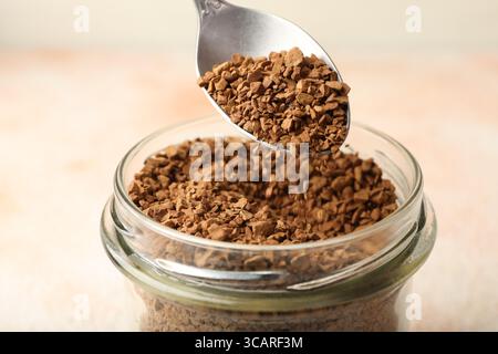 Prendre du café instantané granulé du pot avec cuillère sur fond clair flou, gros plan Banque D'Images