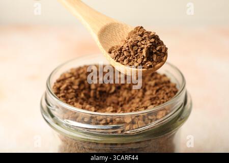 Prendre du café instantané granulé du pot avec cuillère sur fond clair flou, gros plan Banque D'Images