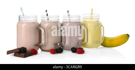 Différents milkshakes savoureux dans des pots mason et ingrédients isolés sur blanc Banque D'Images